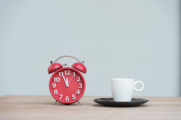 Retro alarm clock with five minutes to twelve o'clock.coffee cup on wooden table .