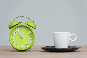 Fototapeta na wymiar Retro alarm clock with five minutes to twelve o'clock.coffee cup on wooden table .