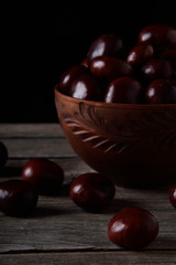 Fresh chestnuts in a bowl on an old wooden table. Group of chestnuts. Chestnuts - fruits horse chestnut - Aesculus hippocastanum. Dark background. Autumn background
