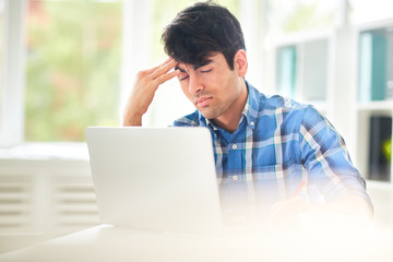 Tired designer touching his forehead in front of laptop