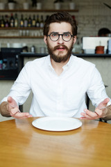 Young man in white shirt sitting by table in cafe with empty plate