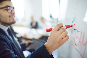 Market analyst making accent on teamwork in the following year while making report by whiteboard