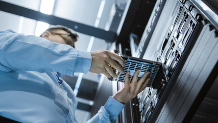 Low Angle Shot In Fully Working Data Center IT Engineer Installs Hard Drive into Server Rack. Detailed and Technically Accurate Footage.
