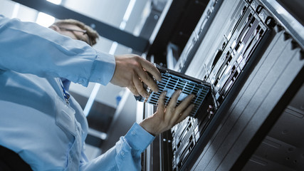Low Angle Shot In Fully Working Data Center IT Engineer Installs Hard Drive into Server Rack....