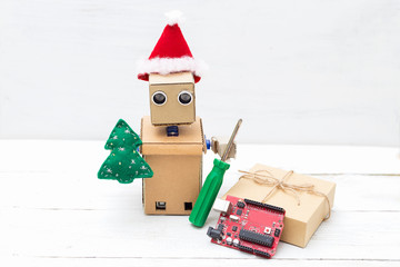 A robot in a santa hat holds a toy of christmas tree and screwdriver. Horizontal photo