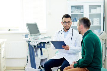 Middle-aged bearded patient having consultation with highly professional physician at modern...