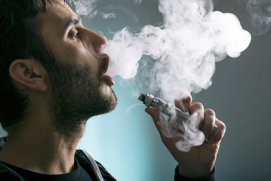 young man vape electronic cigarette cloud by using a mod, smoke tricks of vaping device background. 