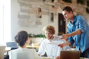Fototapeta premium Group of young business partners discussing contract terms while negotiating in cafe