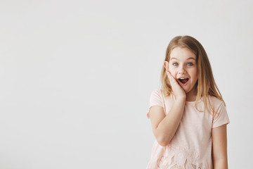 Positive emotions and expressions. Cute little girl looking in camera with happy and excited expression, holding hand on cheek, being surprised to get flowers from boy.