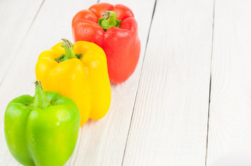 Row of red yellow and green fresh whole raw pepper on old white rustic planks