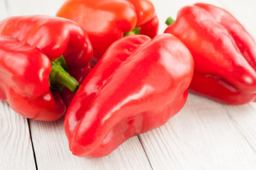 Four fresh red whole raw pepper on old white rustic planks