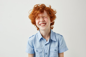 Portrait of joyful little boy with ginger hair and freckles laughing out loud with closed eyes in...