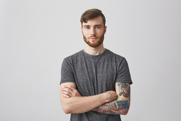 Portrait of beautiful young man with ginger beard and tattooed hand looking in camera with gentle smile and calm expression. - Powered by Adobe