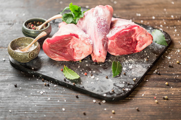 Raw lamb shanks with salt and pepper on stone tray on rustic wooden table. selective focus © jarvna