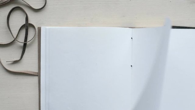 Close up top view on clean white designer wooden table and big a4 notebook with pure white recycled paper sheets turning over and over. Loop video of page turning of personal diary