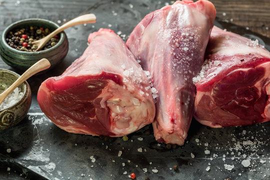 Raw lamb shanks with salt and pepper on stone tray on rustic wooden table. selective focus