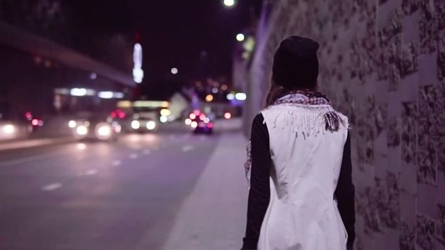 Young woman walking along night city street, slow motion