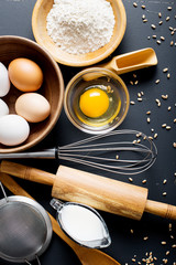 Fototapeta na wymiar Baking ingredients. Bowl, eggs, flour, eggbeater, rolling pin and eggshells on black chalkboard from above.