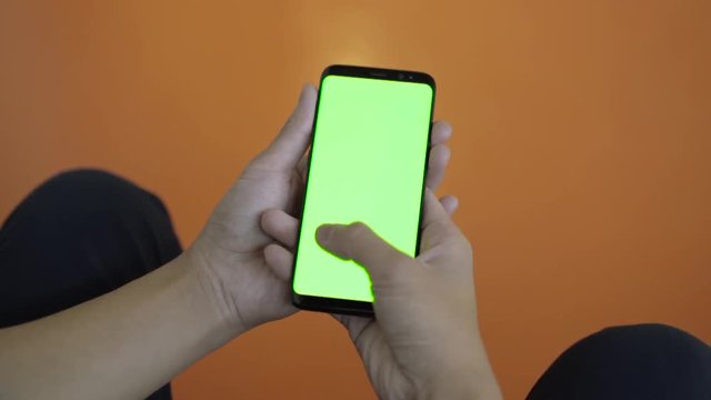 Using mobile phone with green screen in public. Thumb swiping right and left through display