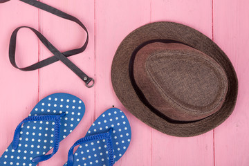 Summer accessories - sun hat, belt and flip flops on pink wooden table