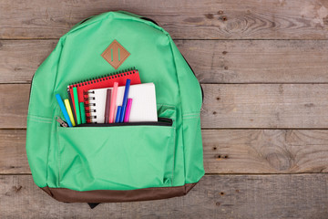 Backpack and school supplies: notepad, felt-tip pens on brown wooden table