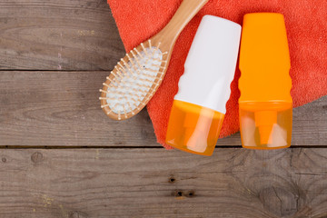 Set of bathing accessories - orange towel, hairbrush and cosmetics for pampering on brown wooden background