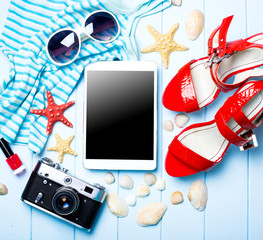 Summer women's accessories: sunglasses, red shoes, dress on blue wood background.