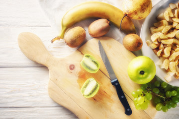 Ingredients for fruit salad. Cutting kiwi