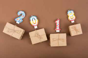 New year concept - gift boxes and text "2018" made of candles on a brown paper background