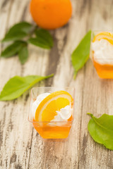 Orange jelly in a cup with whipped cream and orange sliced on black wooden background
