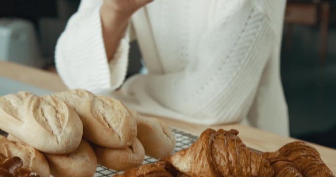 Young attractive woman in a white sweater is picking up and eating a mini croissant in an upscale bakery