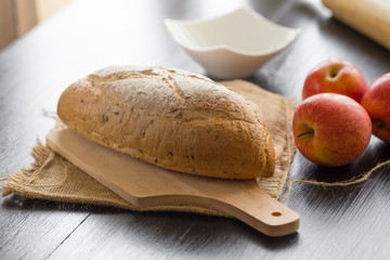 French bread baguette cut on wooden board with knife.  with red apple