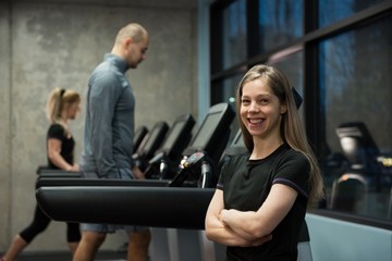 Fototapeta na wymiar Smiling woman standing with people exercising on treadmill