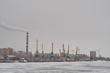 Winter port with frozen water, harbour cranes and smoke pipe. Industrial district