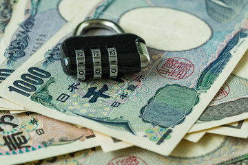 selective focus on combination lockpad on pile of japanese yen banknotes as financial safe haven or security concept