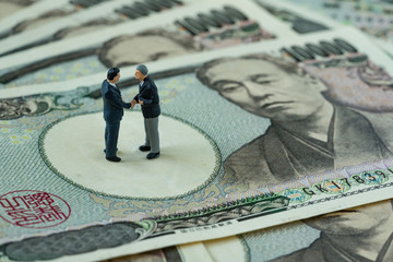Business goals or agreement concept as miniature figure businessmen handshaking and standing on pile of japanese yen banknotes