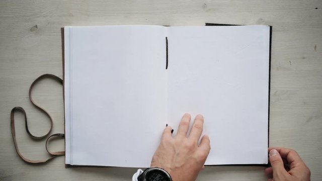 Top view on big a4 notebook with blank mockup papers, isolated on clean white wooden table. Hands turn some pages and hold still. Loop video, education and presentation business concept