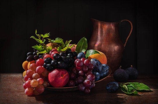Still life with fruits: grape, apple, fig, pear and peach on the antique copper tin plate and a cooper jug near