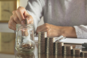 Woman process and drop coin into the glass with stack coins and calculator. Woman working on table.
