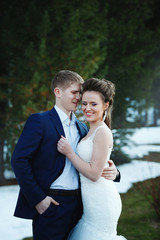 Fototapeta premium Winter wedding outdoors on snow background. Bride and groom are standing and hugging.