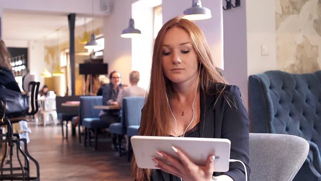 Young, pretty woman with red hair watching movie on tablet sitting in cafe
