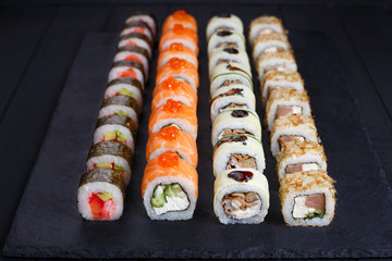 Tasty appetizing  multicolored maki sushi rolls set with wide assortment of fillings, served on black stone slate. Restaurant menu