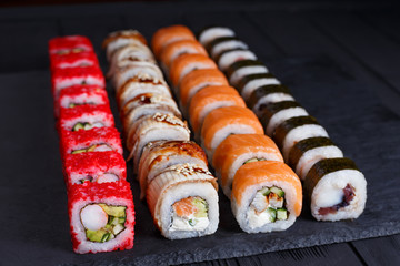 Tasty appetizing  multicolored maki sushi rolls set with wide assortment of fillings, served on black stone slate. Restaurant menu