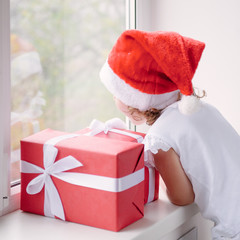 little girl in Santa hat looking out of window next to boxes wit