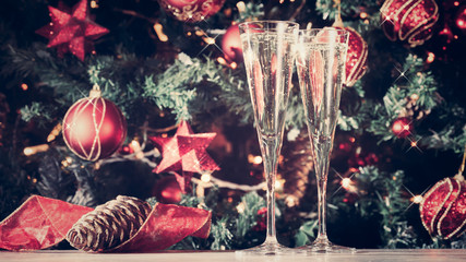 Two glasses of champagne with Christmas tree background and sparkles. Holiday season background....