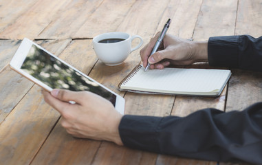 Close up businessman write on notebook and using tablet working in coffee shop.
