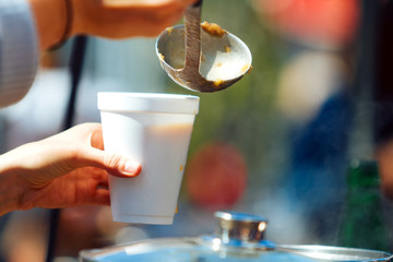Hand of woman serving hot soup in a disposable glass