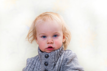 baby (2 years old) blond boy with long hair in a warm gray sweater