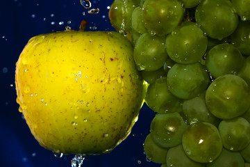 juicy yellow apple and Green grape with water drops on a blue background