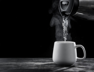 Pouring hot water into into a cup on a black background